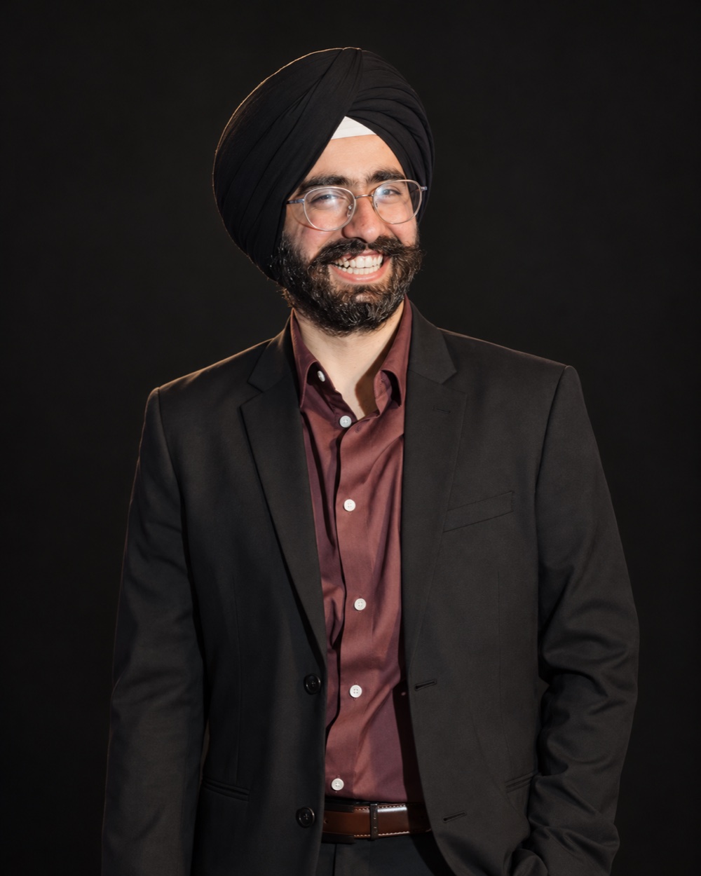Harmandeep Singh smiling, wearing a black turban, glasses, and a black blazer
